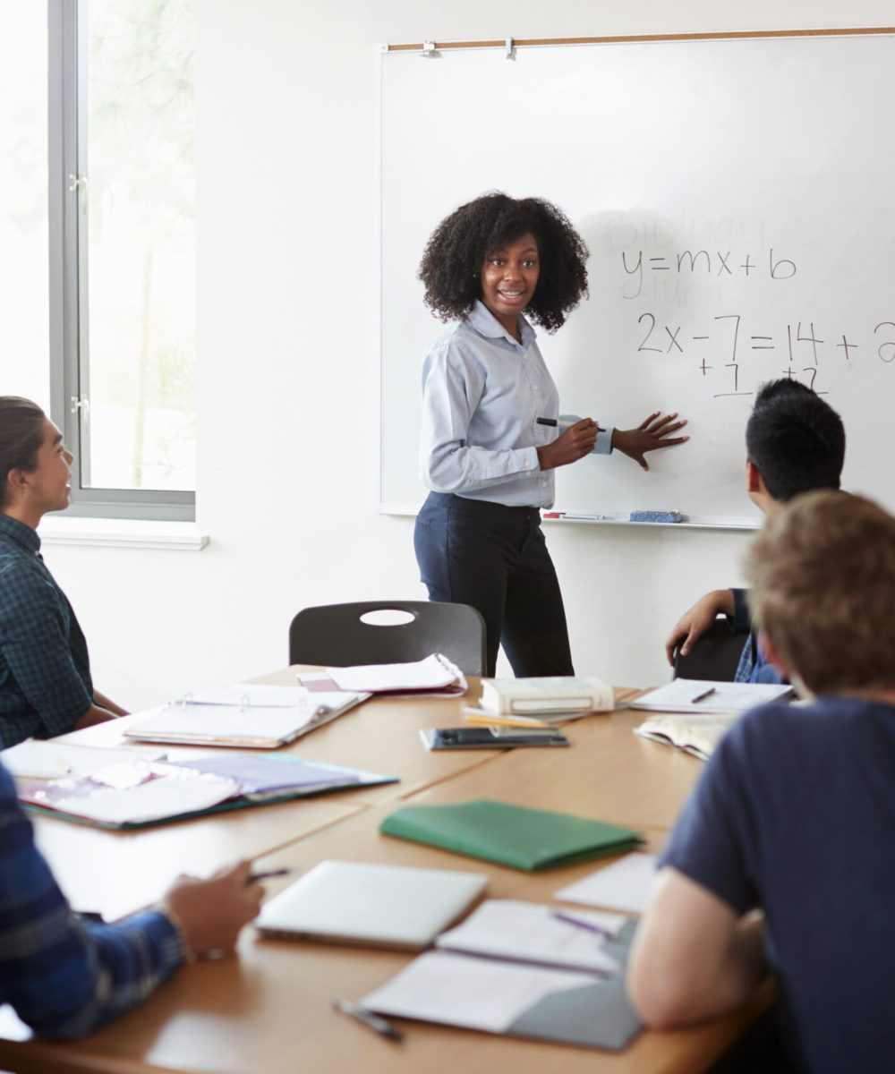 Female High School Tutor At Whiteboard Teaching Maths Class